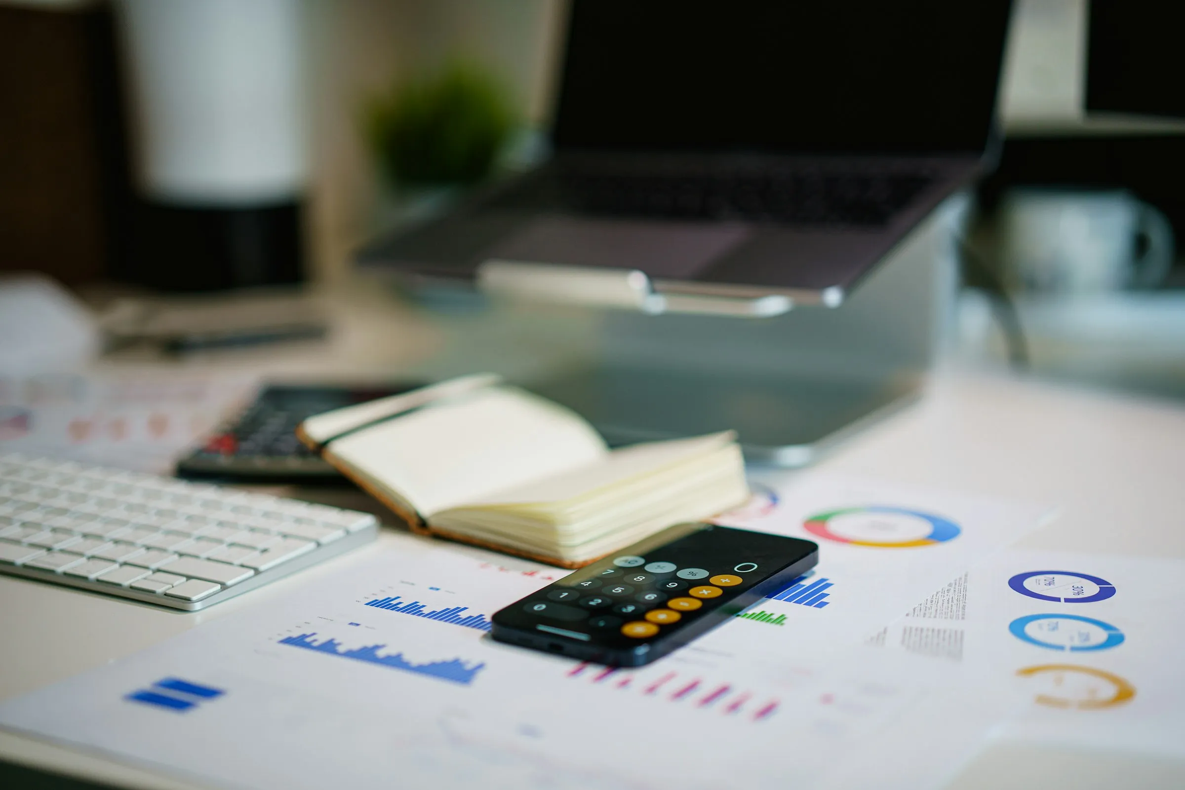 Desk with a laptop, calculator, and printed financial charts and reports